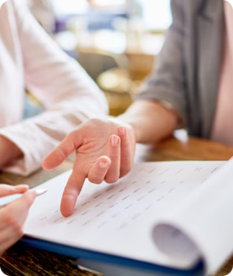 Deux personnes sont assises à une table et examinent un document ; l'une d'elles montre le papier tandis que l'autre tient un stylo, ce qui suggère une discussion ou un accord.