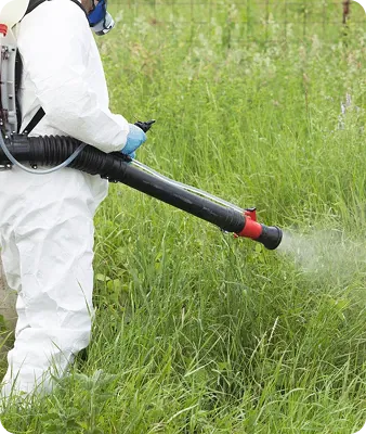 Technicien en combinaison de protection pulvérisant un traitement anti-moustiques en extérieur